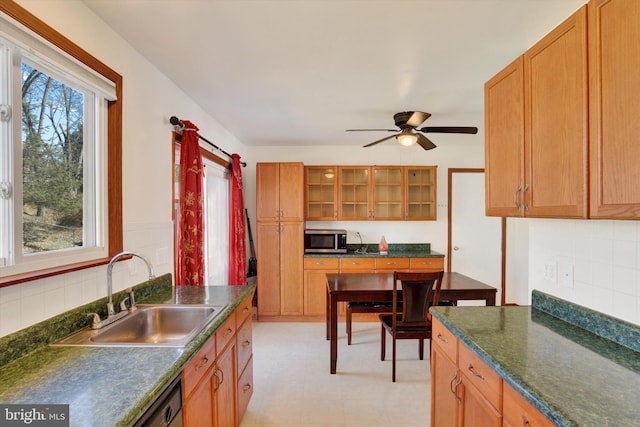 kitchen featuring dark countertops, stainless steel microwave, glass insert cabinets, a ceiling fan, and a sink