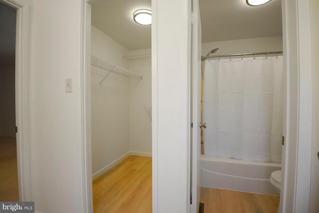 bathroom with shower / bathtub combination with curtain, toilet, wood finished floors, and a spacious closet