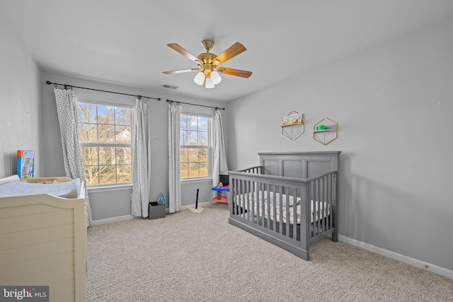 bedroom with baseboards, visible vents, a ceiling fan, light colored carpet, and a nursery area