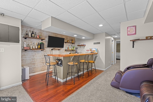 bar with a bar, dark wood-style flooring, a drop ceiling, and baseboards