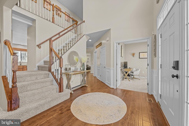 foyer entrance with stairs, a decorative wall, a high ceiling, and wood finished floors