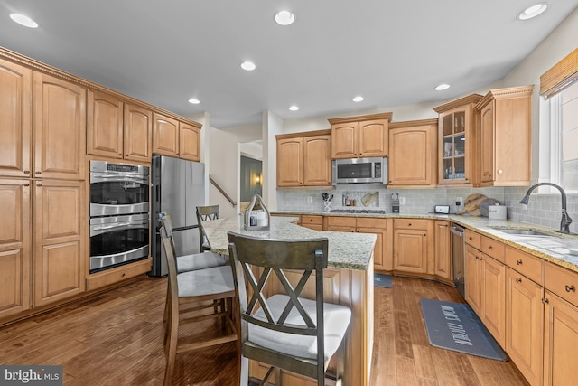 kitchen with glass insert cabinets, light stone counters, a kitchen island with sink, stainless steel appliances, and a sink