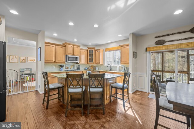 kitchen with a kitchen island, light stone countertops, stainless steel microwave, a kitchen bar, and glass insert cabinets