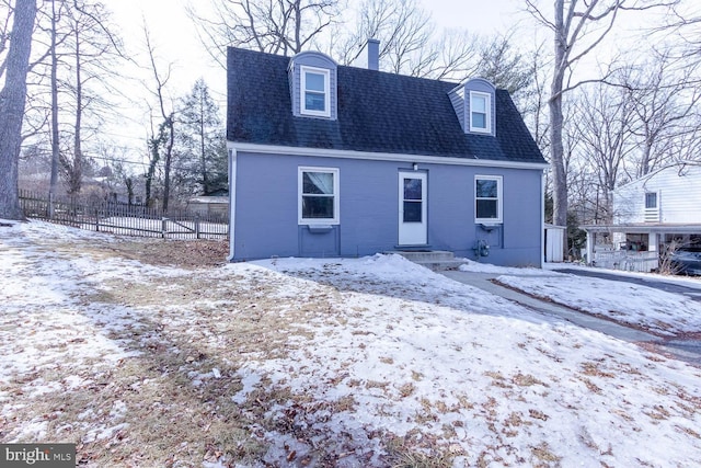 snow covered rear of property with roof with shingles, fence, and brick siding