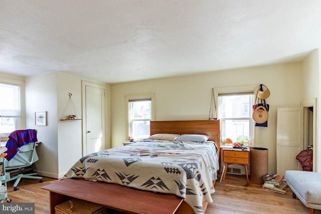 bedroom featuring light wood-style flooring, baseboards, and a textured ceiling