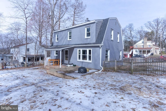 snow covered property with a residential view, roof with shingles, fence, and a gambrel roof