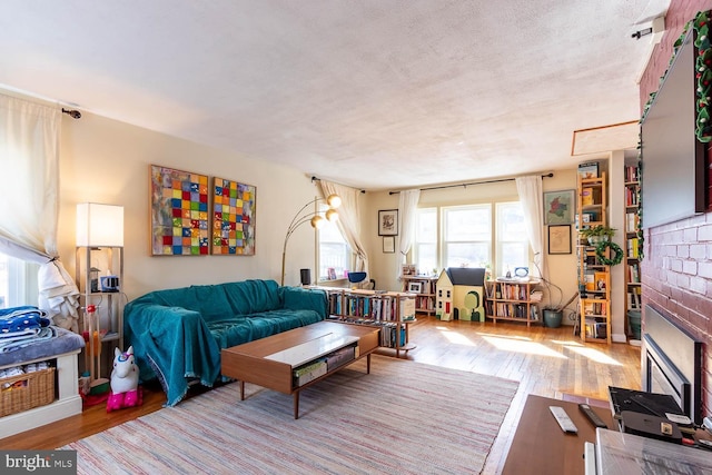 living room featuring light wood-style floors, a brick fireplace, and a textured ceiling