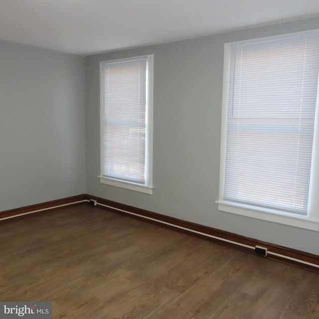 spare room featuring dark wood-type flooring and baseboards