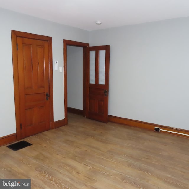 empty room with light wood-type flooring, visible vents, and baseboards