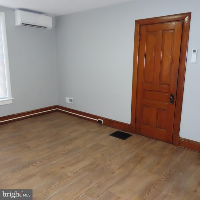 unfurnished room featuring baseboards, visible vents, light wood finished floors, and a wall mounted AC