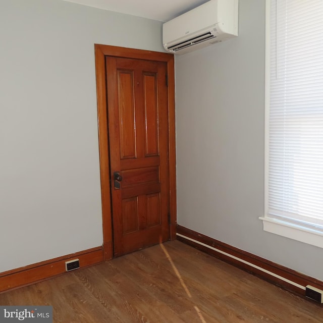 empty room with dark wood-style floors, an AC wall unit, visible vents, and baseboards