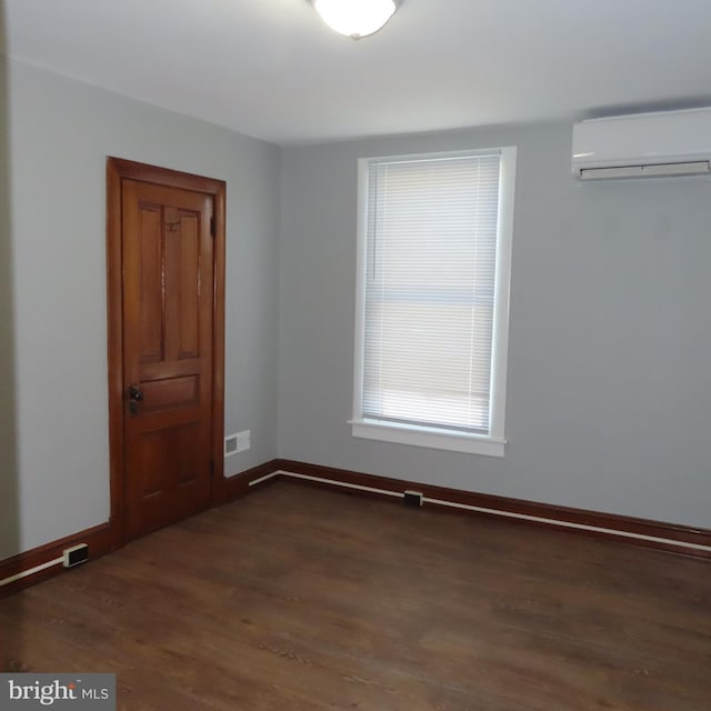 spare room featuring visible vents, baseboards, dark wood-type flooring, and a wall mounted AC