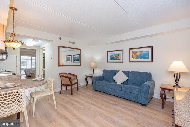 living room featuring baseboards, a textured ceiling, visible vents, and light wood-style floors