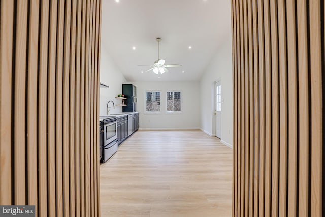 kitchen featuring light wood-style flooring, electric range, a sink, baseboards, and vaulted ceiling