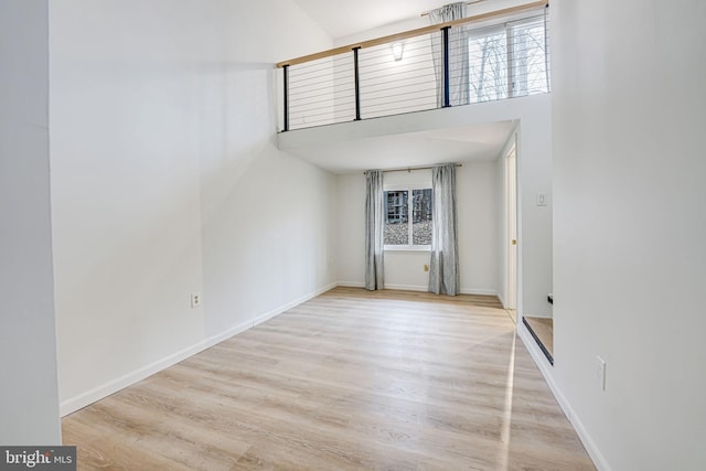 unfurnished room featuring a towering ceiling, light wood-style flooring, and baseboards