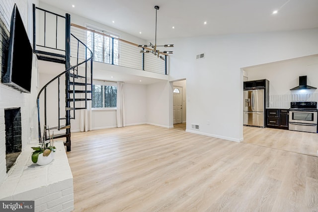 living area featuring a towering ceiling, light wood-style floors, stairway, and visible vents