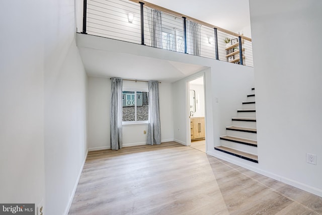 interior space with a high ceiling, light wood-style flooring, stairs, and baseboards