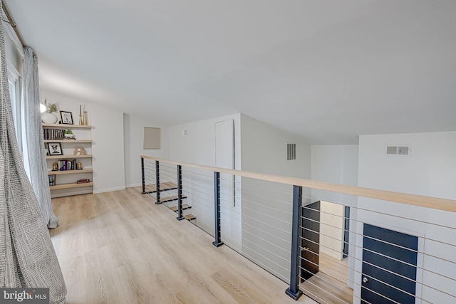 hall featuring light wood-type flooring, visible vents, and an upstairs landing