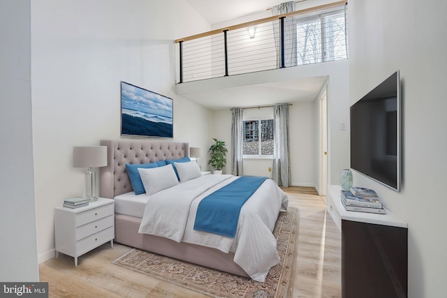 bedroom featuring light wood-type flooring, a towering ceiling, and baseboards