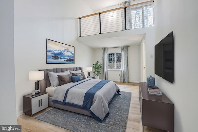 bedroom featuring light wood-type flooring, baseboards, and a high ceiling