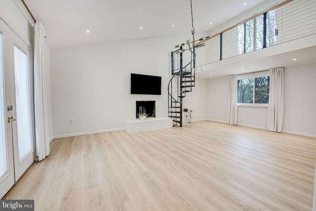 unfurnished living room with a healthy amount of sunlight, a fireplace, light wood-style flooring, and stairs