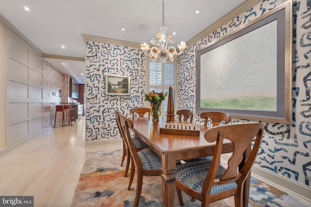 dining space with light wood finished floors, a chandelier, crown molding, and wallpapered walls