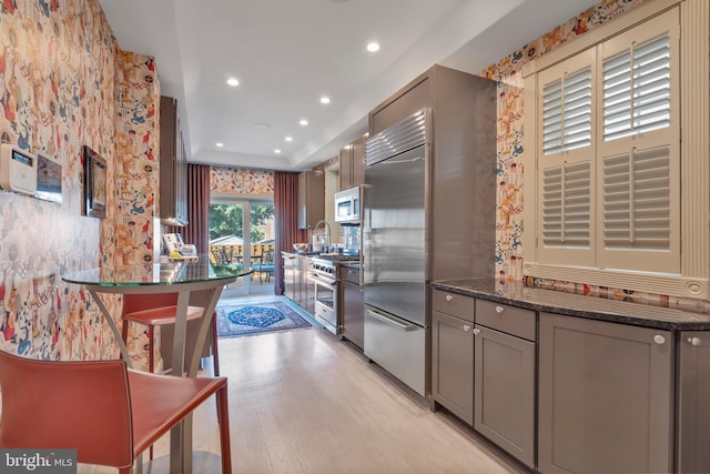 kitchen with light wood-style flooring, recessed lighting, gray cabinets, dark stone countertops, and high end appliances