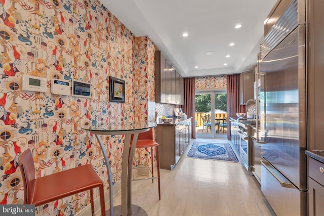 kitchen featuring light wood finished floors, wallpapered walls, recessed lighting, a raised ceiling, and premium appliances