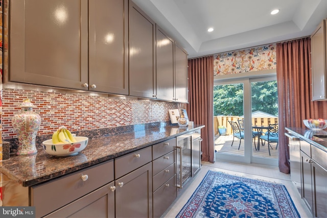 kitchen with backsplash, gray cabinets, dark stone counters, and a tray ceiling