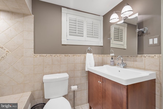 bathroom featuring toilet, tile walls, wainscoting, and vanity