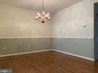 unfurnished dining area featuring dark wood finished floors, baseboards, and an inviting chandelier