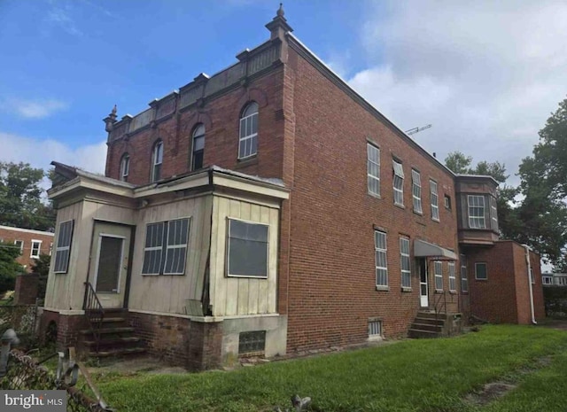 view of side of home featuring entry steps, a lawn, and brick siding