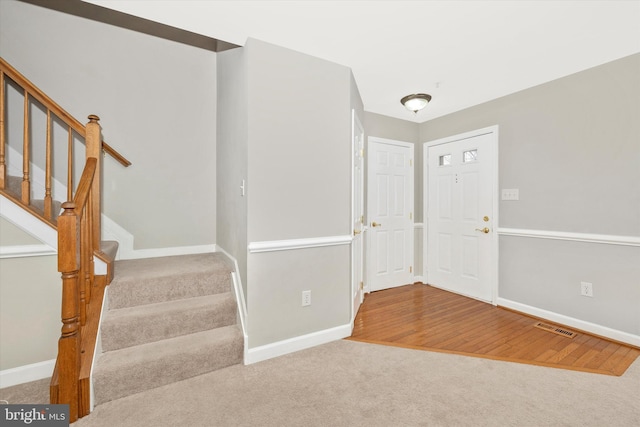 carpeted entrance foyer featuring visible vents, stairs, and baseboards