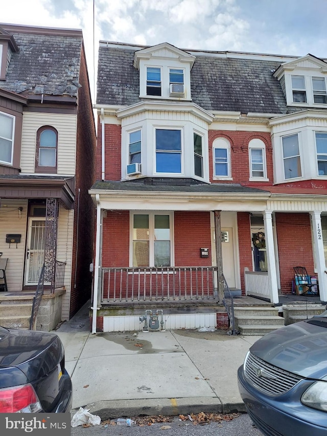 multi unit property featuring mansard roof, a porch, cooling unit, and brick siding