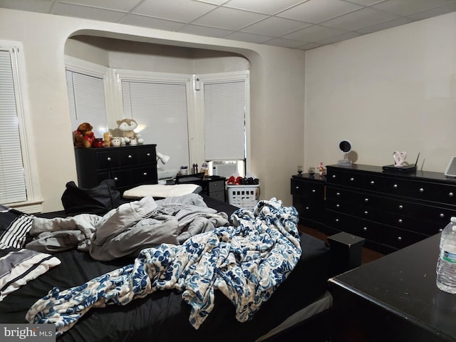 bedroom featuring arched walkways, a drop ceiling, and cooling unit