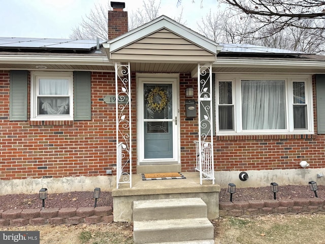 doorway to property featuring brick siding, a chimney, and solar panels