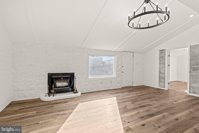 unfurnished living room featuring a chandelier, lofted ceiling, a wood stove, and wood finished floors