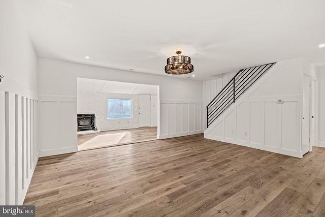 unfurnished living room featuring light wood-style flooring, stairway, a wood stove, a decorative wall, and recessed lighting