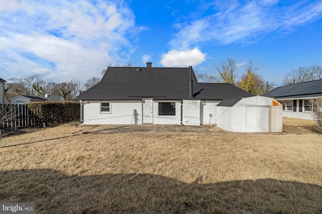 rear view of property featuring a chimney, a lawn, fence, a shed, and an outdoor structure