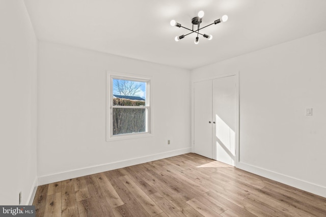 empty room featuring light wood-style floors, baseboards, and an inviting chandelier