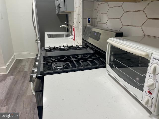 kitchen featuring stainless steel gas range, light countertops, gray cabinetry, and wood finished floors