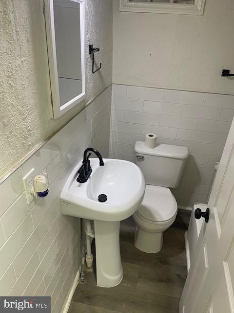 bathroom with a wainscoted wall, a textured wall, wood finished floors, and toilet