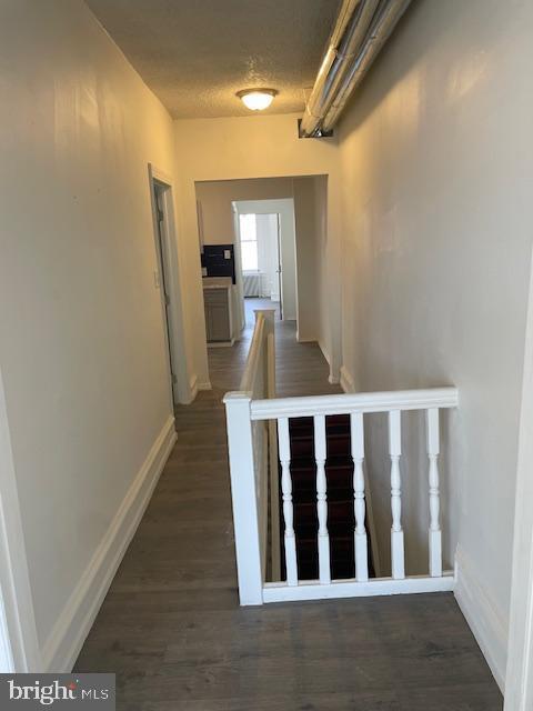 hall featuring dark wood-style floors, an upstairs landing, and baseboards