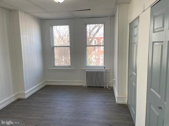 unfurnished room featuring radiator, dark wood-style floors, baseboards, and a paneled ceiling