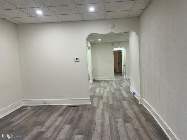 spare room with dark wood-style floors, arched walkways, a paneled ceiling, and baseboards