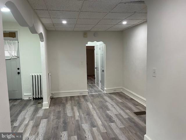 spare room featuring arched walkways, baseboards, radiator heating unit, and wood finished floors