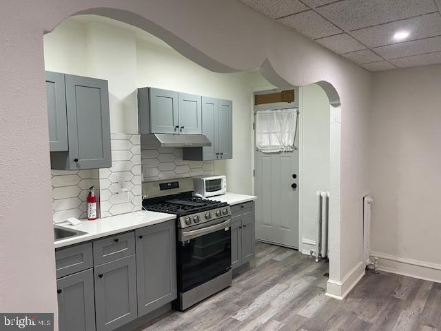 kitchen with a paneled ceiling, light countertops, white microwave, stainless steel gas stove, and wood finished floors