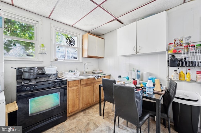 kitchen with light countertops, black gas range, brown cabinetry, white cabinetry, and a sink