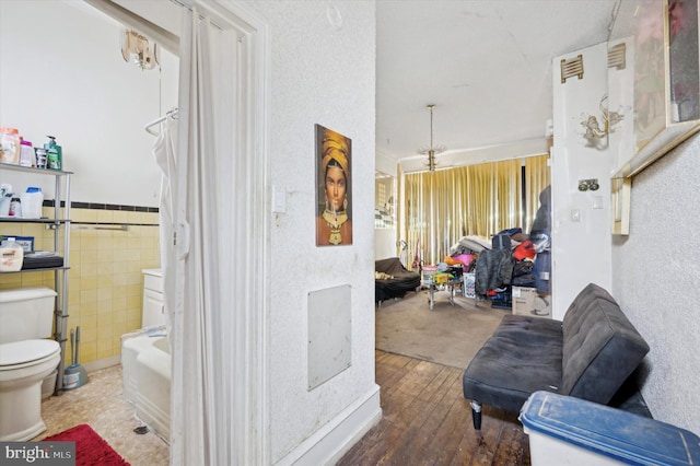 corridor featuring a wainscoted wall, wood finished floors, and tile walls