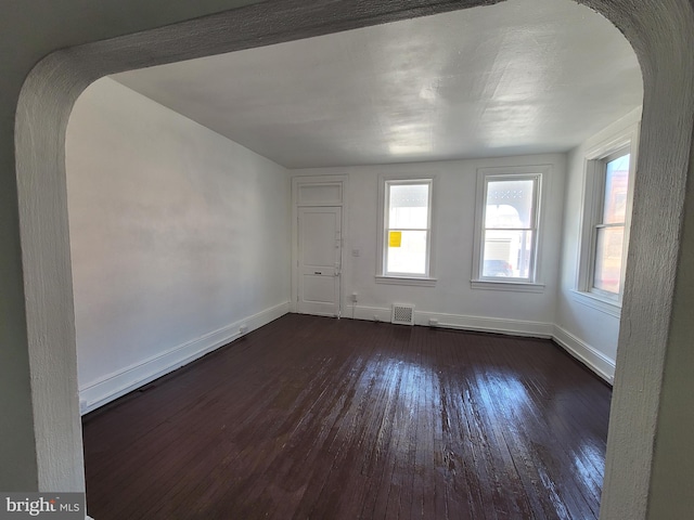 spare room with dark wood-style floors, arched walkways, visible vents, and baseboards